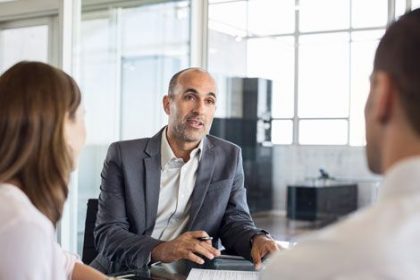 A financial advisor meets with a couple, illustrating the importance of qualified trainers and assessors in the vet sector.
