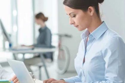 A businesswoman uses a laptop for vet compliance tasks in a bright office.