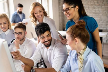 A team discusses VET compliance around a computer in a bright office.