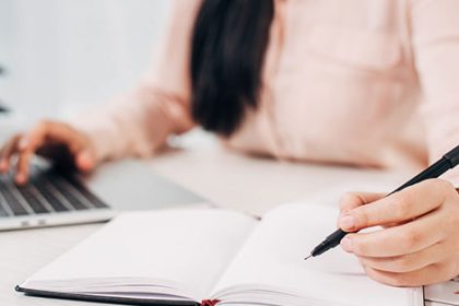 A person writing notes in a notebook while using a laptop for vet training.
