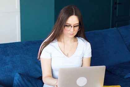 A woman comfortably uses a laptop for online learning in a home office setting.