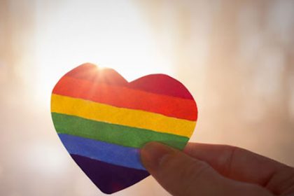 A hand holding a rainbow heart represents inclusivity in Relationships and Sexuality education.