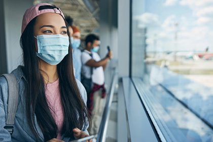 A masked passenger looks out from an airport window, reflecting the increase in international student arrivals.