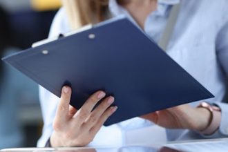 An office worker reviews documents on a clipboard, relating to vet compliance.