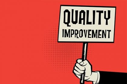 A hand holds a brightly colored sign displaying 'QUALITY IMPROVEMENT', relating to vet compliance.